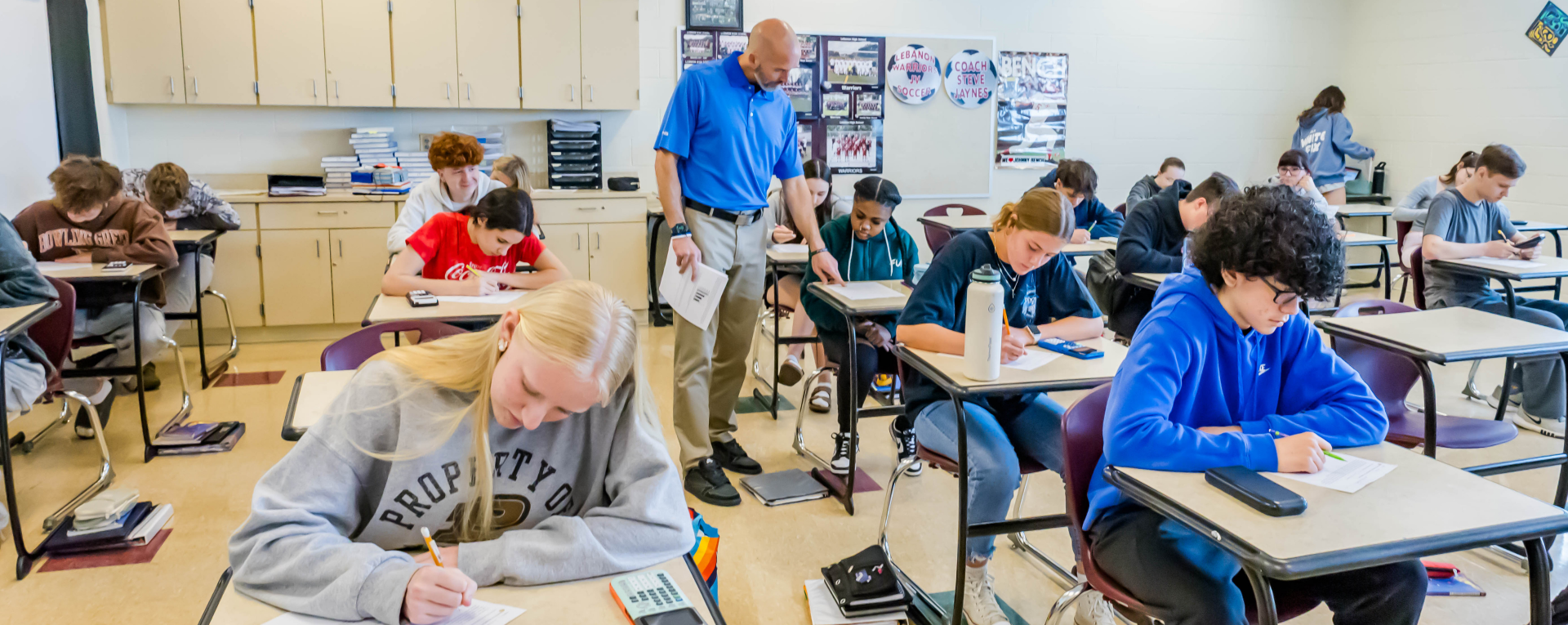 a teacher by a student desk in a classroom